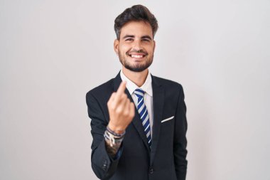 Dövmeli, takım elbiseli ve kravatlı genç İspanyol bir adam seni buraya davet ediyor. Mutlu bir şekilde karşılamaya ve gülümsemeye davet ediyor. 