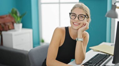 Ofiste gülümseyen bilgisayar kullanan genç sarışın iş kadını.