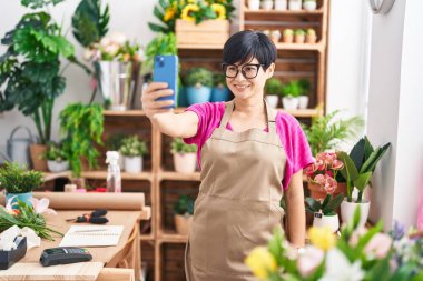 Orta yaşlı Çinli kadın çiçekçi çiçekçide akıllı telefondan selfie çeker.