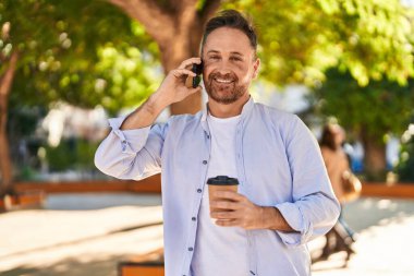 Kafkasyalı genç adam akıllı telefondan konuşuyor parkta kahve içiyor.