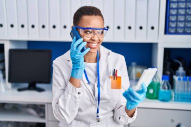 Akıllı telefondan konuşan Afrikalı Amerikalı kadın bilim adamı laboratuarda örnek arıyor.