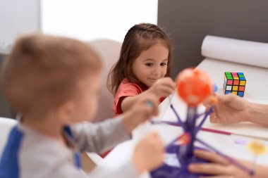 Adorable girl and boy sitting on table learning of planets at kindergarten