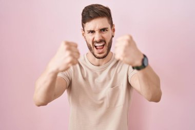 Pembe arka planda sakallı İspanyol bir adam öfkeyle bağırırken kızgın ve kızgın yumruklarını kaldırıyor. öfke ve agresif konsept. 