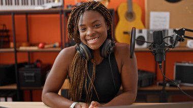 Müzik stüdyosunda gülümseyen kulaklık takan Afrikalı Amerikalı kadın müzisyen.