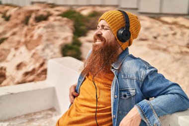 Young redhead man smiling confident listening to music at street