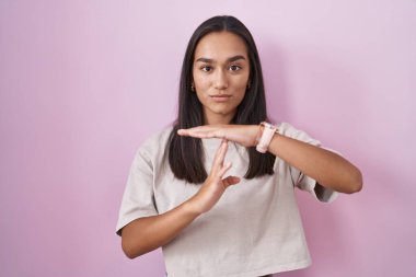 Pembe arka planda dikilen genç İspanyol kadın elleriyle jest yapıyor, hayal kırıklığına uğramış ve ciddi bir yüz ifadesi var. 