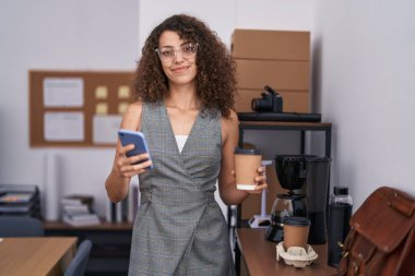 Genç, güzel İspanyol iş kadını. Akıllı telefon kullanıyor. Ofiste kahve içiyor.