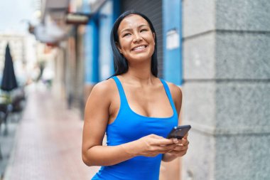 Sokakta akıllı telefon kullanarak gülümseyen güzel Latin bir kadın.