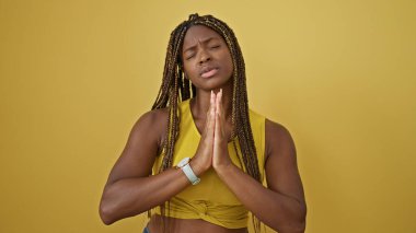 Afrikalı Amerikalı bir kadın izole edilmiş sarı arka plan için dua ediyor.
