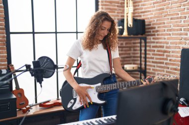 Genç, güzel, İspanyol bir müzisyen müzik stüdyosunda gitar çalarken gülümsüyor.