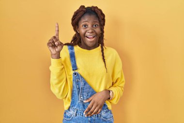 African woman standing over yellow background pointing finger up with successful idea. exited and happy. number one. 