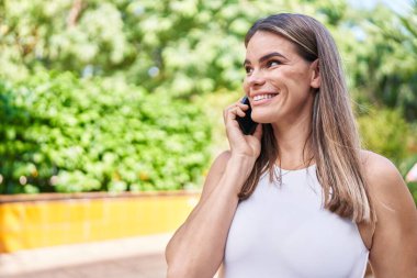 Genç, güzel İspanyol kadın gülümsüyor. Parktaki akıllı telefondan konuşuyor.