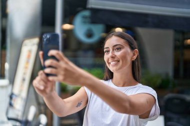 Genç, güzel, İspanyol bir kadın kahve dükkanının terasında kendinden emin bir şekilde selfie çekiyor.