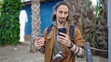 Genç İspanyol turist parkta elinde kahve tutan akıllı telefon kullanıyor.