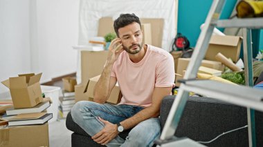 Yeni evinde ciddi bir ifadeyle koltukta oturan İspanyol asıllı genç adam.