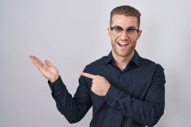 İzole edilmiş arka planda duran genç beyaz adam kameraya hayret ediyor ve gülümsüyor.. 