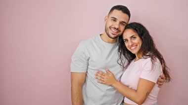 Erkek ve kadın çift gülümsüyor, kendilerine güveniyorlar, pembe arka planda sarılıyorlar.