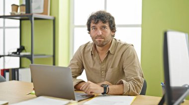 Genç İspanyol iş adamı ofiste ciddi suratlı dizüstü bilgisayar kullanıyor.