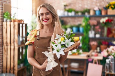 Young beautiful hispanic woman florist holding bouquet of flowers at flower shop