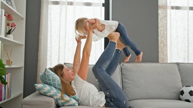 Kafkasyalı anne ve kız kanepede rahat bir şekilde uzanıp evlerinin sıcaklığında oynayıp gülümsüyorlar.