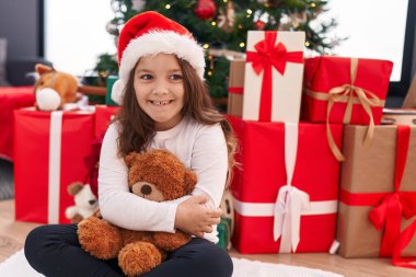 Sevimli İspanyol kız oyuncak ayıyı kucaklıyor. Evde Noel ağacının yanında oturuyor.