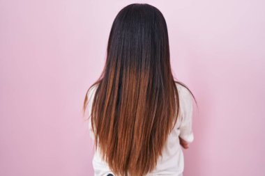 Pembe arka planda duran genç Arap kadın kollarını kavuşturup arkasına bakıyor. 