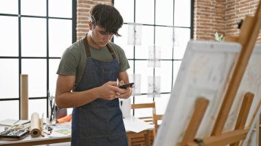 Sanatına dalmış genç bir İspanyol sanatçıyı büyüleyici bir şekilde görmek, dikkatle bir sanat stüdyosunun içindeki akıllı telefonuyla meşgul olmak.