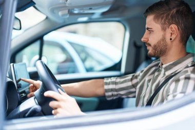 Sokakta bilgisayar GPS 'ine dokunarak araba kullanan beyaz bir genç.