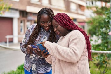 Sokakta akıllı telefon ve kredi kartı kullanan Afrikalı Amerikalı kadın arkadaşlar