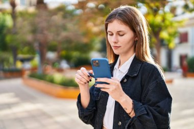 Parkta akıllı telefonu ayna niyetine kullanan genç sarışın bir kadın.