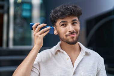Young arab man smiling confident listening audio message by the smartphone at street