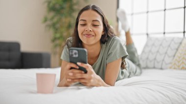 Afrika kökenli Amerikalı kadın, yatakta uzanmış, akıllı telefon kullanıyor.