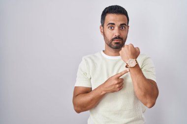 Sakallı İspanyol bir adam tecrit edilmiş arka planda dikiliyor. Aceleyle saati, sabırsızlığı izliyor ve rahat bir ifadeyle kameraya bakıyor. 