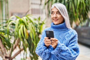Middle age grey-haired woman smiling confident using smartphone at street