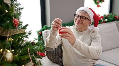 Orta yaşlı, kır saçlı adam evde Noel ağacı süslüyor.