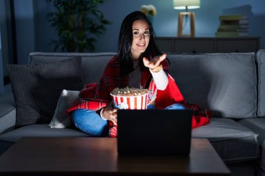 İspanyol kadın kanepede film seyrederek patlamış mısır yiyor. Neşeli bir şekilde gülümsüyor. Yardım eli uzatıyor ve kabul ediyor.. 