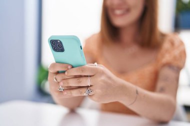 Young redhead woman using smartphone sitting on table at home