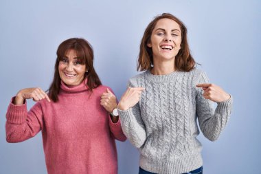 Anne ve kızı mavi arka planda duruyor. Yüzünde bir gülümsemeyle, gururlu ve mutlu birini işaret ediyor.. 