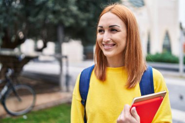 Young caucasian woman student smiling confident holding books at park