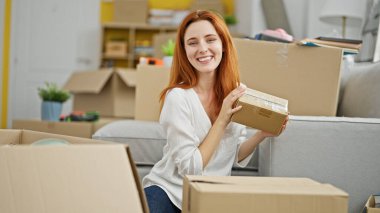 Genç kızıl saçlı kadın yeni evinde kendine güvenen bir paket tutuyor.