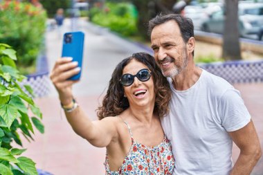 Erkek ve kadın çift birbirlerine sarılıyorlar. Parkta akıllı telefondan selfie çekiyorlar.