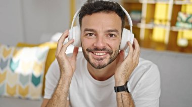 Genç İspanyol adam evdeki kanepede oturmuş müzik dinliyor.