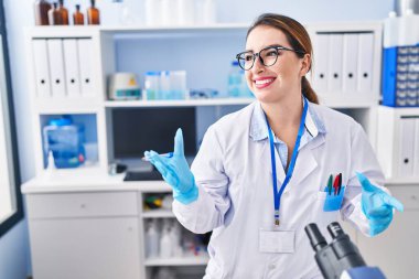 Genç ve güzel İspanyol bilim kadını laboratuarda mikroskop kullanarak konuşuyor.
