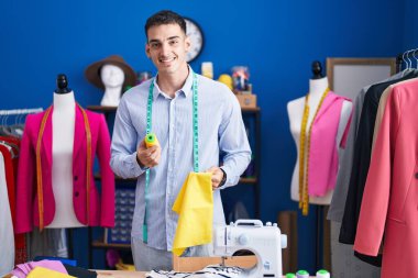 Genç İspanyol terzi gülümseyerek dikiş atölyesinde kumaş ve iplik tutuyor.