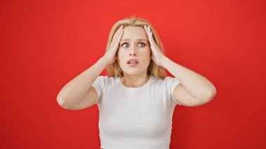 Sarışın genç bir kadın, izole edilmiş kırmızı arka planda sürpriz jest yapıyor.