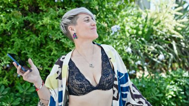 Genç bir kadın parkta akıllı telefondan müzik dinliyor.