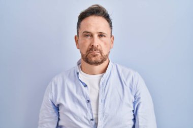 Mavi arka planda duran orta yaşlı, beyaz bir adam depresyonda ve endişe içinde, kızgın ve korkmuş bir şekilde ağlıyor. hüzünlü ifade. 