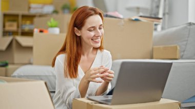 Genç kızıl saçlı kadın yeni evinde dizüstü bilgisayar kullanıyor.