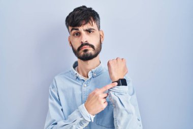 Mavi arka planda duran sakallı genç İspanyol adam acele ederek saati, sabırsızlığı ve rahat bir ifadeyle kameraya bakıyor. 