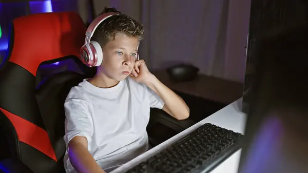 可爱的金发男孩流光溢彩 全神贯注地玩着一个未来派的电子游戏 晚上在他的数字游戏室里用科技产品现场直播 面容专注而轻松 — 图库照片